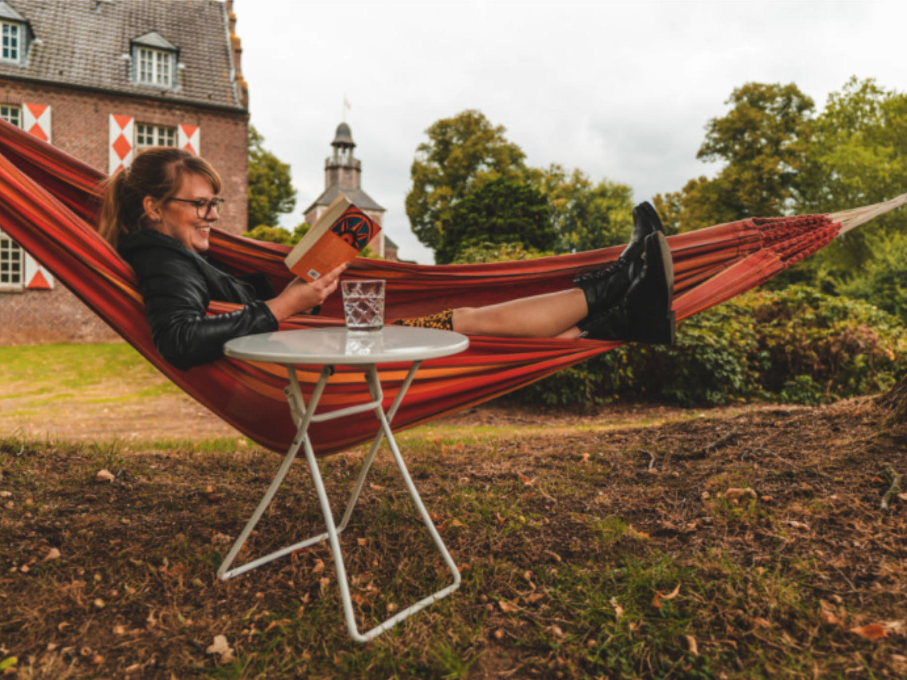 schloss-hertefeld-arrangement-oblomow_foto-@gymifilms Frau liegt in einer Hängematte und liest ein Buch